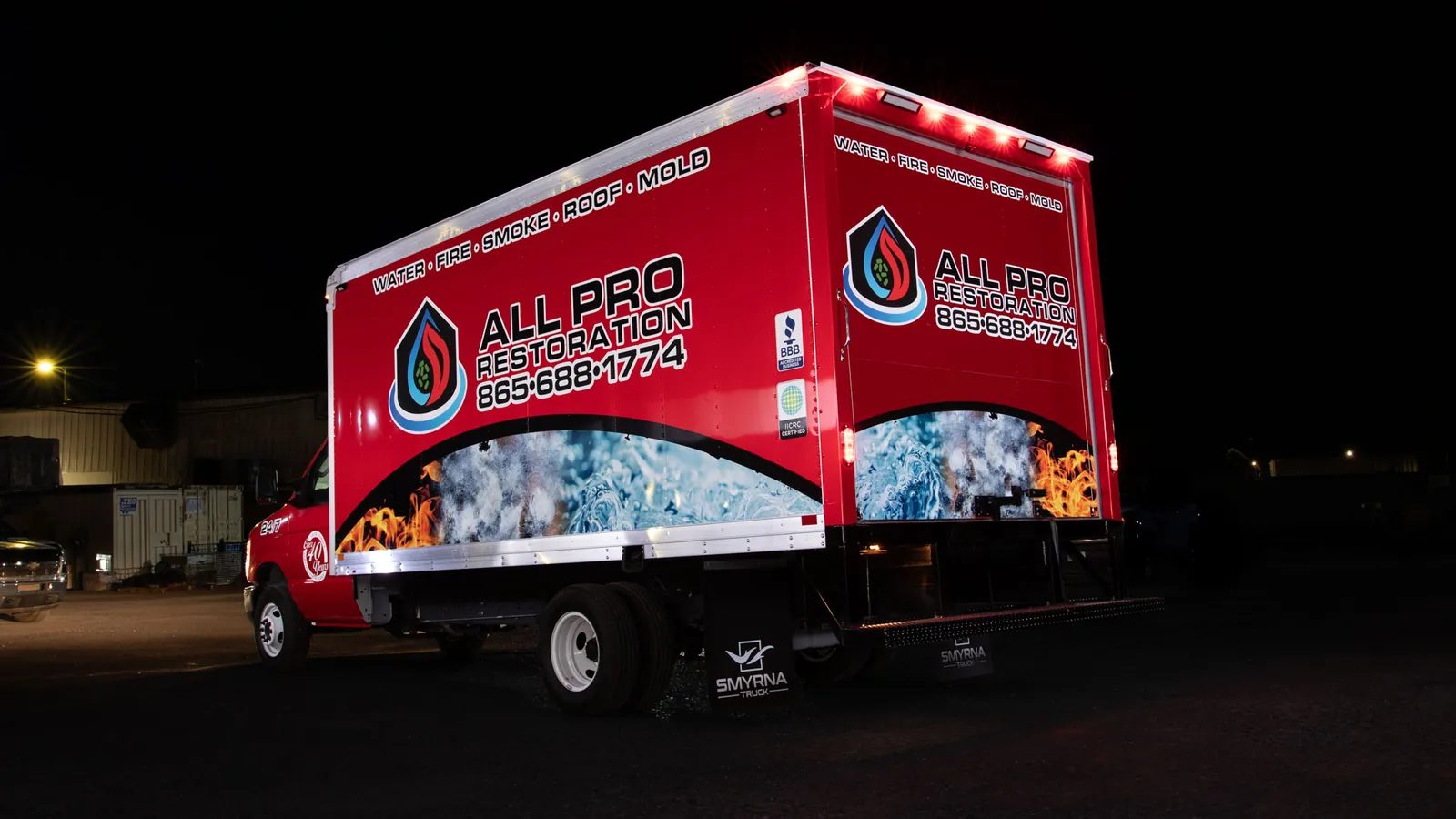 Red All Pro Restoration box truck with a full printed wrap, photographed at night with only the red marker lights on